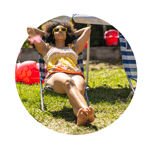 A woman in sunglasses laying back on a deck chair bathing in the sun on green grass