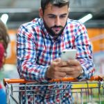 Customer pushing shopping cart whilst using mobile phone amid cost of living crisis