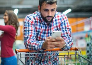 Customer pushing shopping cart whilst using mobile phone amid cost of living crisis